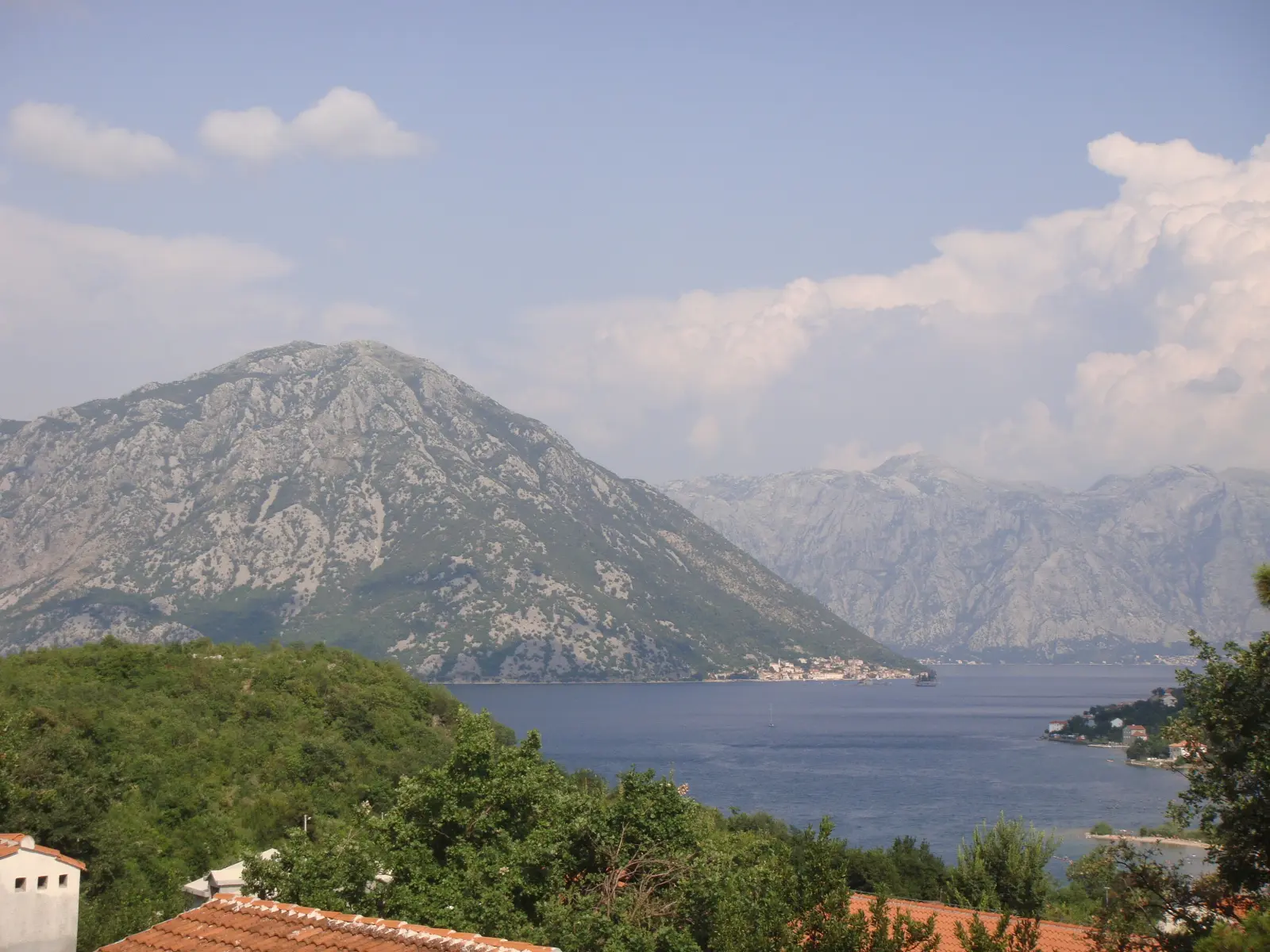 Blick auf Morinj aus dem Hinterland: Steinhäuser, grüne Berghänge und die Bucht von Kotor im Hintergrund