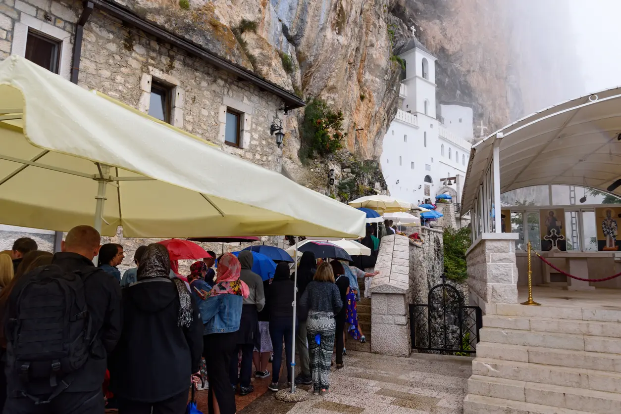 Panoramski pogled na bijeli Manastir Ostrog uklesan u vertikalnu stijensku liticu Ostroških greda, sa dolinom Zete u pozadini